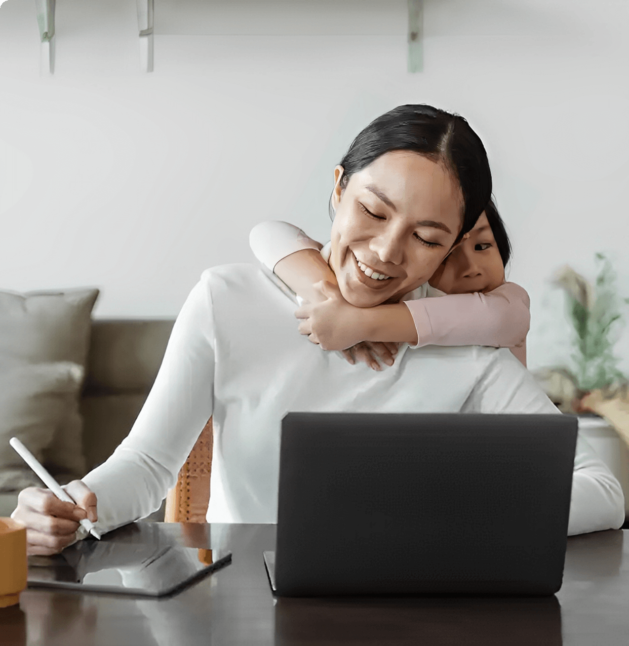 Mother working, child hugging her from behind.